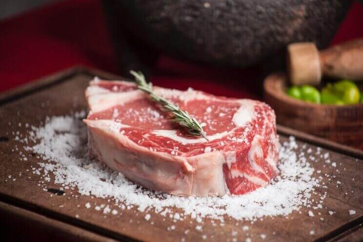 Piece of raw meat covered in salt and thyme sat on top